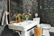 a creative bathroom with chalkboard walls, a tiled floor, a large pedestal sink, a toilet, a tree stump and gold fixtures
