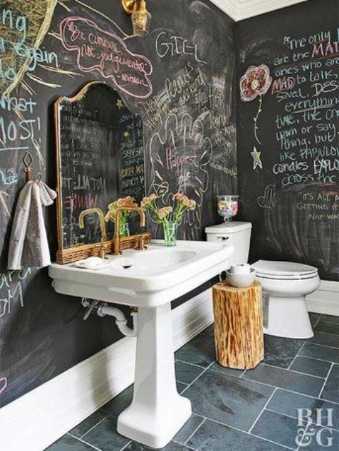 a creative bathroom with chalkboard walls, a tiled floor, a large pedestal sink, a toilet, a tree stump and gold fixtures