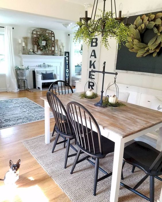 a cute farmhouse dining nook with a chalkboard, a greenery wreath, a wooden dining table, black chairs and a chandelier