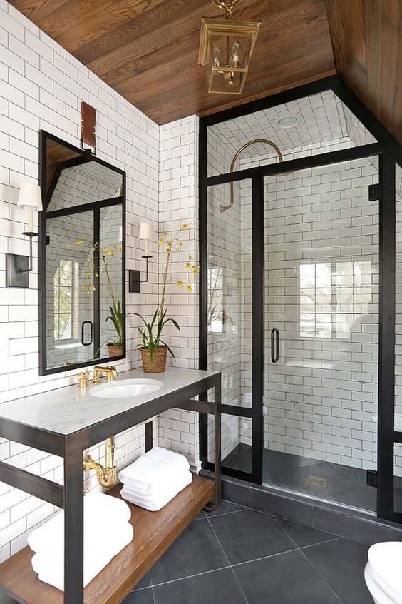 a farmhouse bathroom clad with white subway and black square tiles, a vanity and a shower space done with black frame glass doors
