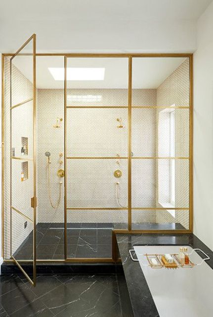 a glam and sophisticated bathroom done with black marble and penny tiles, with a shower space with gold framed glass doors