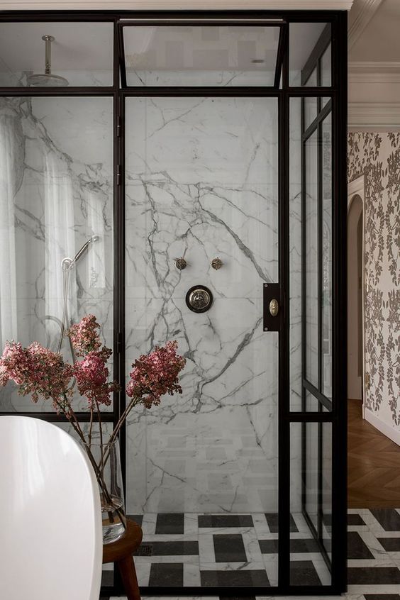 a glam black and white bathroom with white marble tiles and black and white ones, black frame glass doors and an oval tub