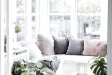 a lovely Nordic sunroom in white, with a built-in sectional sofa with pastel pillows, potted plants and a low wooden coffee table