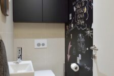 a minimalist black and white powder room with a chalkboard wall, a wall-mounted sink, a sleek black storage unit