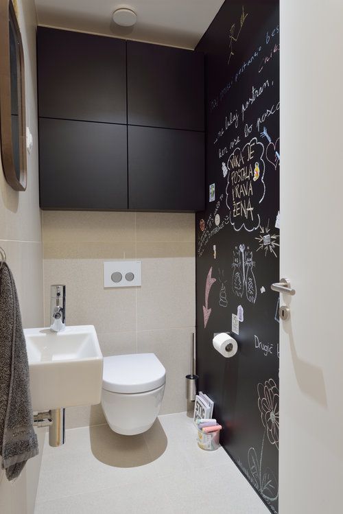 a minimalist black and white powder room with a chalkboard wall, a wall-mounted sink, a sleek black storage unit