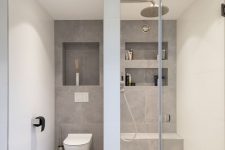 a minimalist neutral bathroom with neutral and grey tiles, a shower space with niches, a seamless glass door and neutral appliances