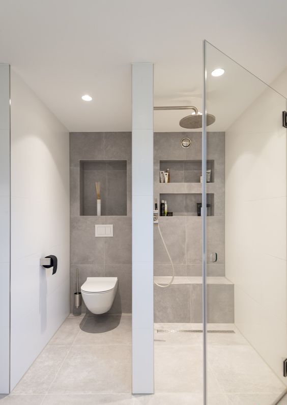 a minimalist neutral bathroom with neutral and grey tiles, a shower space with niches, a seamless glass door and neutral appliances