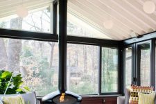 a modern and chic sunroom with neutral furniture, a black suspended fireplace, potted plants and a white coffee table