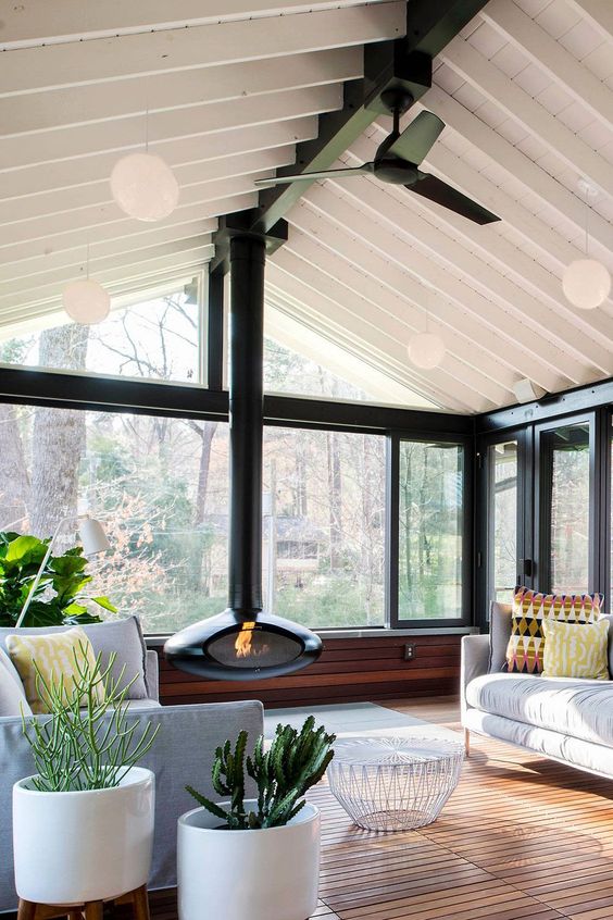 a modern and chic sunroom with neutral furniture, a black suspended fireplace, potted plants and a white coffee table