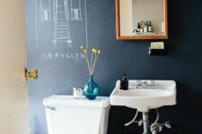 a modern bathroom with a black chalkboard accent wall, a white toilet and a wall-mounted sink, a mirror in a wooden frame