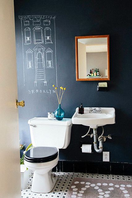 a modern bathroom with a black chalkboard accent wall, a white toilet and a wall-mounted sink, a mirror in a wooden frame