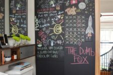 a modern bathroom with a chalkboard accent wall, a black tile floor, bookshelves, a mirror, a white toilet and fun decor on the wall