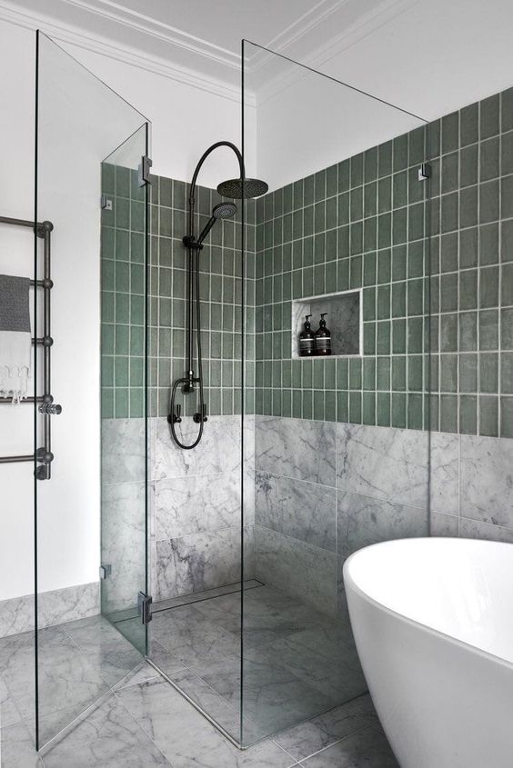 a modern bathroom with white marble and green tiles, an oval tub, a shower space with clear glass seamless doors