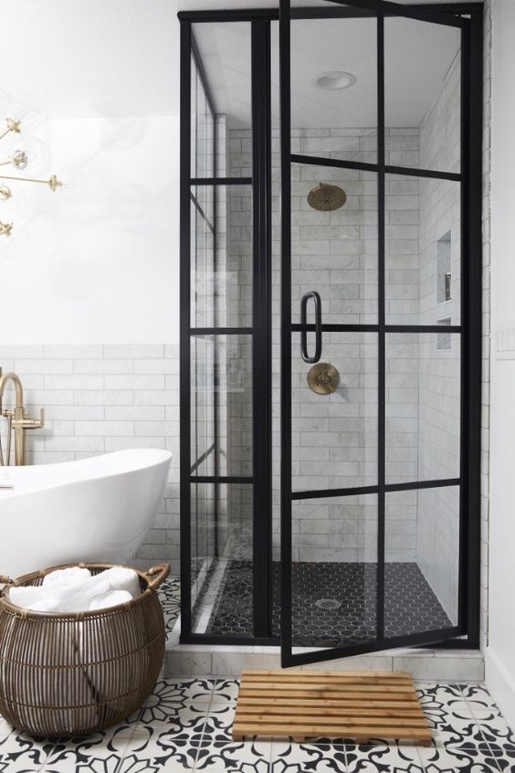 a modern black and white bathroom with a shower space with black French doors, patterned and black tiles, a tub and a basket