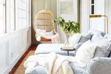 a modern coastal sunroom with striped daybeds, white pillows and blankets, a hanging rattan chair and greenery