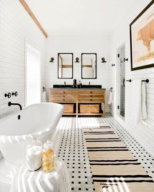 a modern farmhouse bathroom with black and white tiles on the floor, white ones on the wall, an oval tub and a wooden vanity