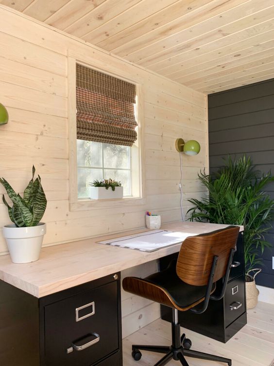 a modern farmhouse home office with the walls, ceiling and floor clad with wood, a contrasting desk and potted greenery