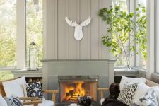 a modern farmhouse sunroom nook with a fireplace, wooden furniture with white upholstery, greenery and a skull