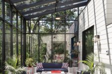 a modern fully glazed sunroom with white furniture and navy upholstery, potted plants and bright red touches here and there