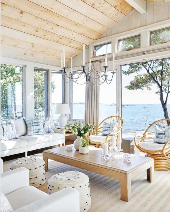 a modern neutral sunroom with a sea view, white seating furniture, rattan chairs, a low coffee table and a vintage chandelier