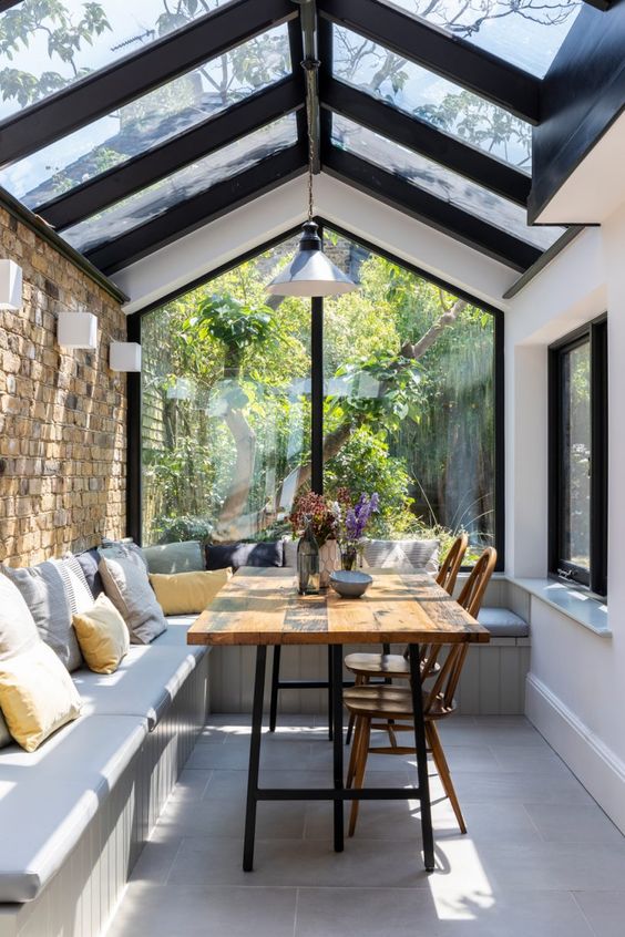 a modern sunroom that is a dining space, with a built-in bench, a dining table and vintage chairs is cool and cozy