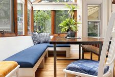 a modern sunroom with a built-in bench with navy upholstery, a dark-stained table and white chairs and a glazed roof