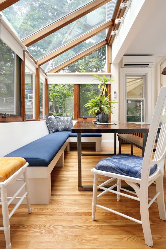 a modern sunroom with a built-in bench with navy upholstery, a dark-stained table and white chairs and a glazed roof