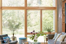 a modern sunroom with a grey sofa, black leather chairs, a low coffee table, potted plants and colorful pillows and blankets