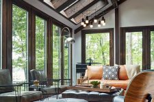 a modern sunroom with skylights and a series of windows, an amber leather sofa and grey and black leather chairs, a bold rug and cool lamps