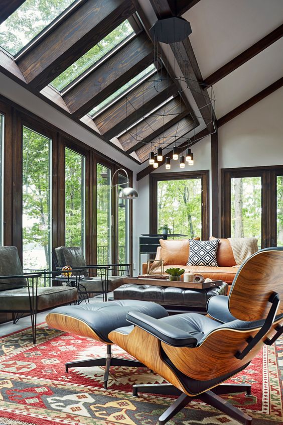 a modern sunroom with skylights and a series of windows, an amber leather sofa and grey and black leather chairs, a bold rug and cool lamps