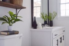 a modern white farmhouse bathroom with a modern vanity, a dark framed mirror, stained shelves and much light