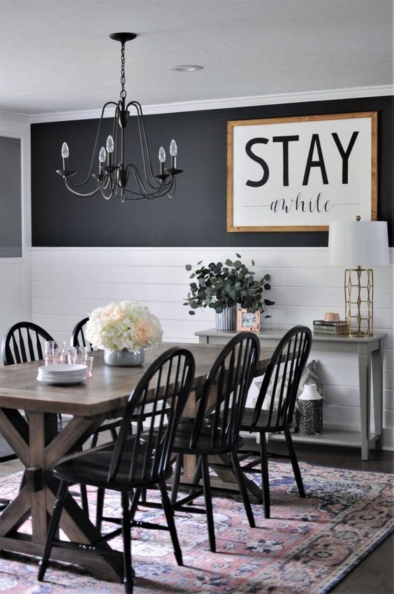 a monochromatic farmhouse dining room with a black and white wall, a large sign, a stained table and black chairs