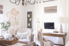 a neutral and cozy farmhouse home office with a wooden desk and a table, neutral upholstered chairs, a vintage chandelier, macrame art on the wall