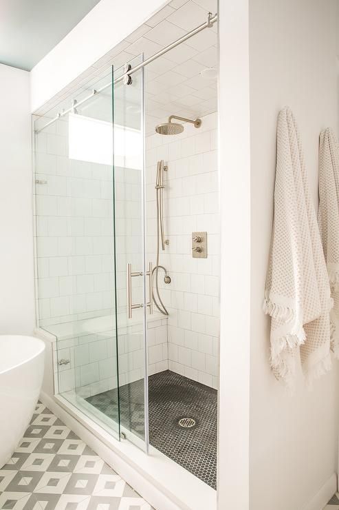 a neutral bathroom with white square, black penny and geo tiles, a shower space with sliding doors and an oval tub