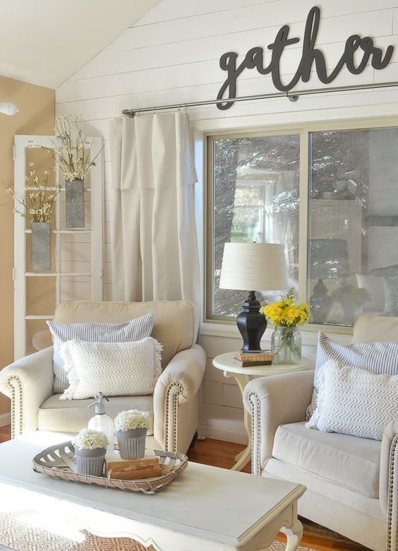 a neutral farmhouse sunroom with elegant vintage furniture, a lamp, blooms and a calligraphy sign over the chairs