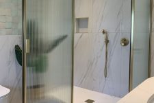 a refined bathroom with white marble tiles, a shower space with ribbed glass doors in gold frames and gold fixtures is wow