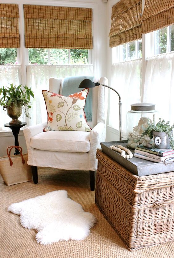 a rustic sunroom with shades, vintage and rattan furniture, layered rugs, potted greenery and lamps