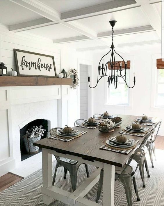 a simple modern farmhouse dining area with a white fireplace, signs and pumpkins, a wooden table and metal chairs