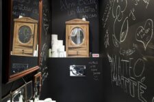a small and cool powder room with black chalkboard walls, a wall-mounted sink, a mirror in a frame and a tiled floor