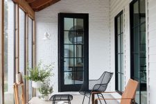 a small and elegant modern sunroom with a coffee table, a black metal and an amber leather chair, potted plants and a rug