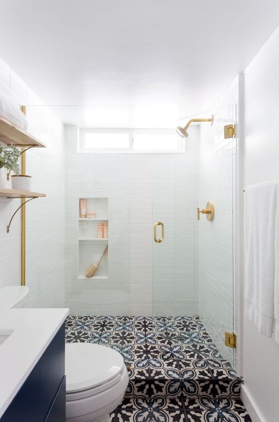 a small contemporary bathroom with white tiles in the shower, patterned tile floor, a navy vanity and a shower space with clear and seamless glass doors with a gold handle