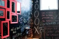 a small modern powder room with black chalkboard walls, a white wall-mounted sink, a white toilet and a gallery wall of pink framed mirrors