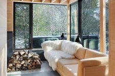 a small modern sunroom with a light-colored sofa and a side table, firewood stacked and a couple of black lamps