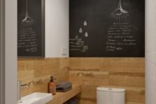 a small powder room with a chalkboard wall, timber paneling, a built-in sink, a mirror and a sconce