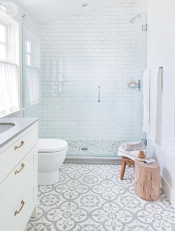 a small serene bathroom with white subway tiles, patterned ones on the floor, a shower space with clear glass doors and a handle