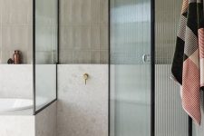 a soothing and welcoming bathroom with grey skinny and white stone tiles, black frame ribbed glass doors with a single knob