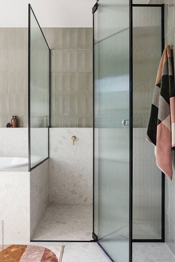 a soothing and welcoming bathroom with grey skinny and white stone tiles, black frame ribbed glass doors with a single knob
