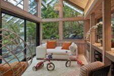 a stylish attic sunroom with a white sofa, a woven chair and a pendant one, some orange touches and pendant lamps