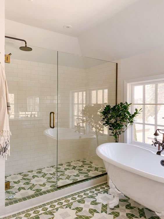 a stylish bathroom with white subway and green and white printed tiles, a clawfoot tub and a shower with glass doors and brass handles