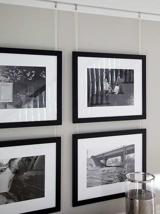 a stylish gallery wall with photos in black frames hanging on wire from above is a chic decor idea